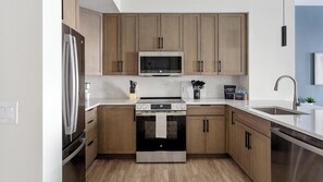 A modern kitchen with wooden cabinets, stainless steel appliances, and a white countertop. - Landing | Spectacular 1BD, Pool (Philadelphia)