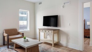 A living room with a sofa, a coffee table, a TV on a stand, and a window with blinds. - Landing | Spectacular 1BD, Pool (Philadelphia)