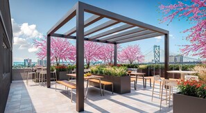 A rooftop patio with a pergola, seating, and cherry blossom trees. - Landing | Chic 1BD, Pool (Philadelphia)