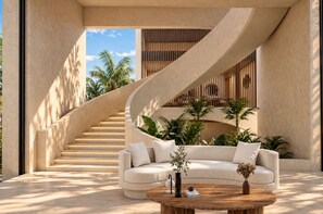 Un interior moderno con una escalera curva, un sofá color crema y una mesa de centro con objetos decorativos.