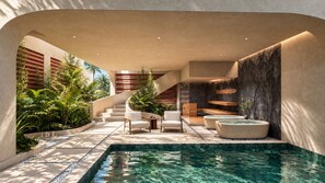 A modern indoor pool area with a clear pool, seating, and a staircase leading to upper levels.