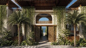 A covered walkway with palm trees, a patterned archway, and a view of the sea.