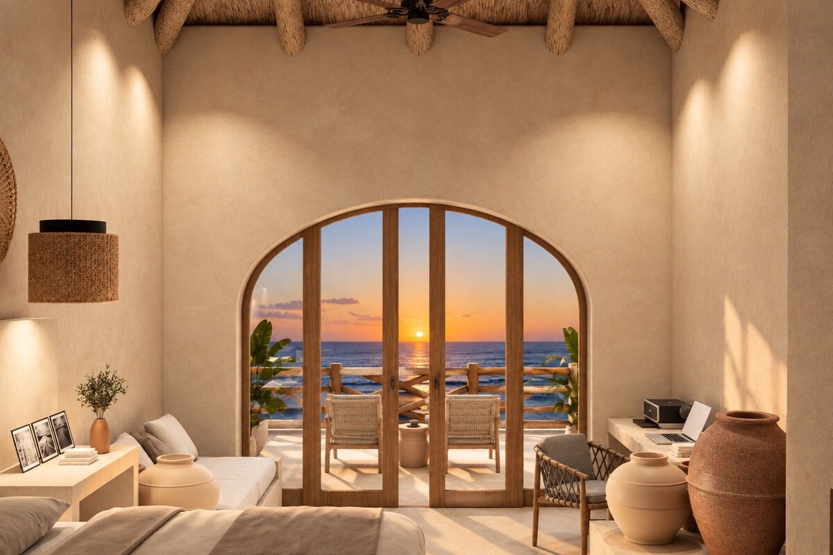 Una habitación con vista al atardecer sobre el océano, una cama, un escritorio con una computadora portátil y una silla.