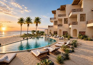 Un resort con piscina, sillas de descanso, palmeras y vistas al océano al atardecer.