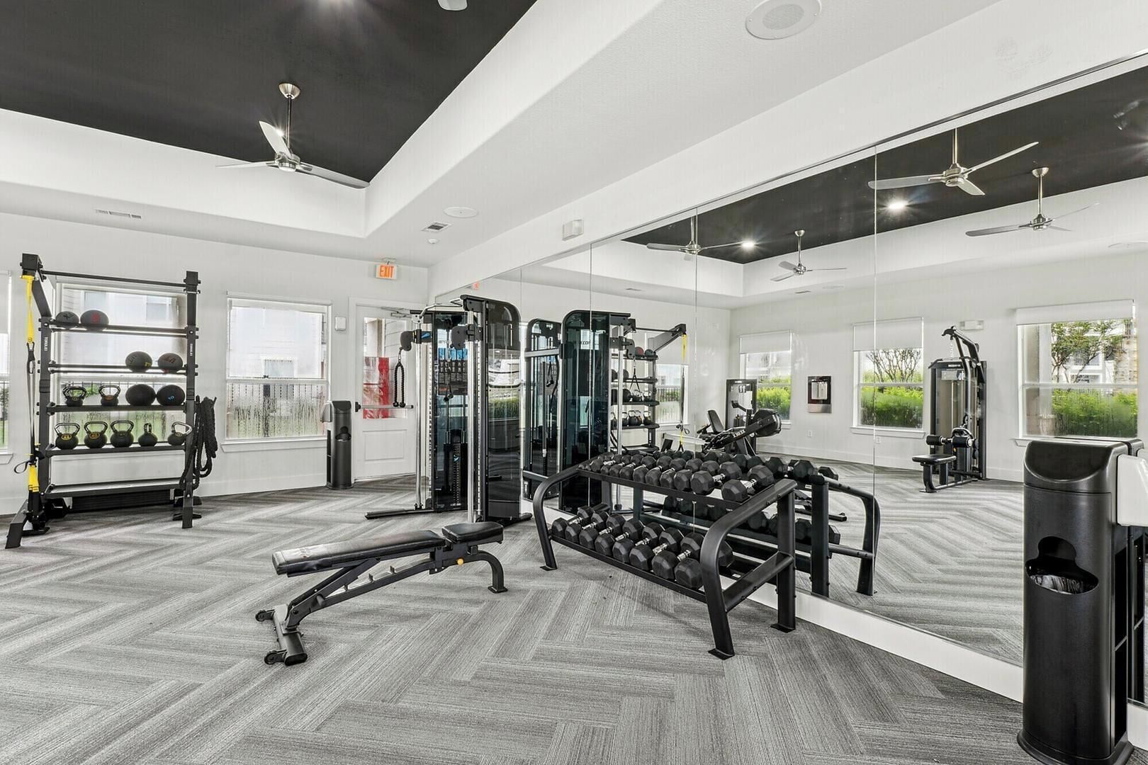 Een fitnessruimte met trainingsapparatuur, spiegels en ramen.