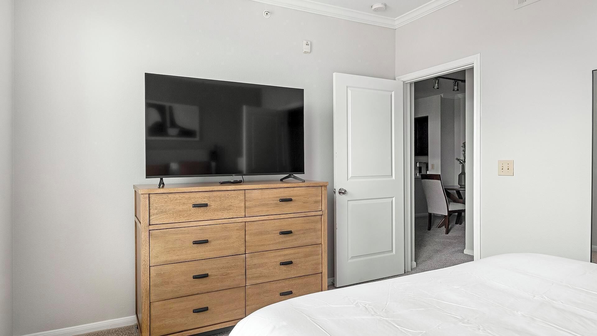 Een slaapkamer met een houten dressoir, een flatscreen televisie, een witte deur en een bed.