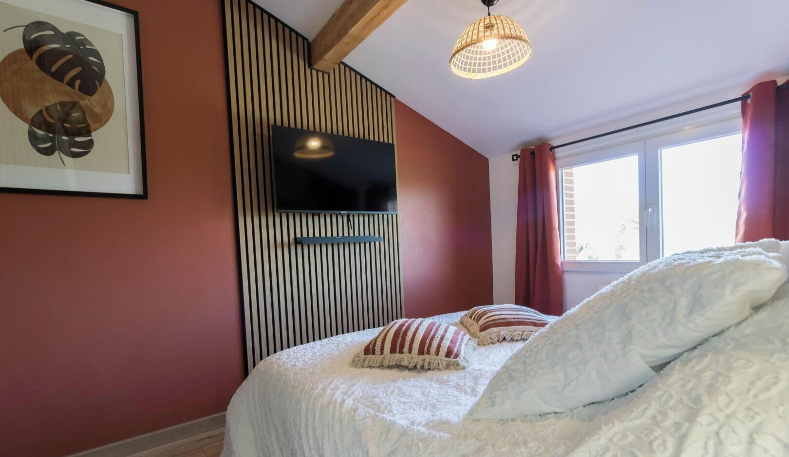 A bedroom with a bed, a TV mounted on the wall, a window with curtains, and a ceiling light fixture.