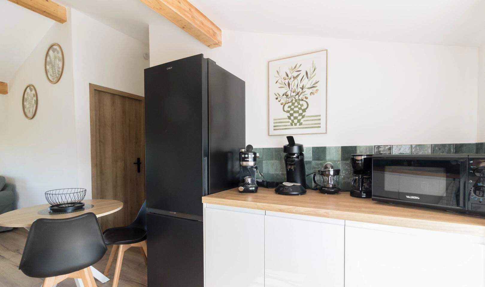 A compact kitchen with a black refrigerator, a coffee maker, a microwave, and a framed artwork on the wall.