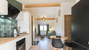 Eine kompakte Küche mit Herd, Backofen und modernen Geräten. Es gibt eine Essecke mit Tisch und Stühlen sowie eine Wohnfläche mit Sofa und Fernseher.