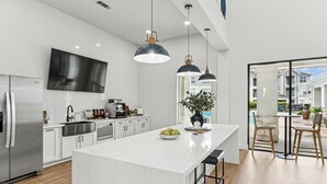 Una cucina moderna con una grande isola, elettrodomestici in acciaio inossidabile, illuminazione a sospensione e vista su una zona residenziale.
