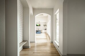 A hallway leading to a kitchen with a tiled backsplash, wooden flooring, and a window on the right. - Landing | Stylish 2BD, Game Room, Clubhouse (Houston)