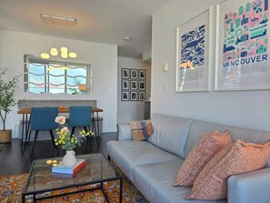 A modern living room with a sofa, coffee table, and a dining area with chairs and a table.