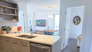 A modern kitchen with a built-in dishwasher, a dining area with a table and chairs, and a hallway leading to a bedroom. - Mountain View l Gym, Patio & Parking, 5 mins to DT (Vancouver)