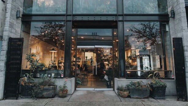 A modern building with large glass windows, a visible entrance, and potted plants outside. - Mountain View l Gym, Patio & Parking, 5 mins to DT (Vancouver)