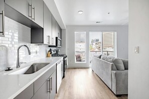 A modern kitchen with a sink, stove, and cabinets, leading to a balcony with a sofa. - Landing | Spectacular Studio in Central City (Salt Lake City)