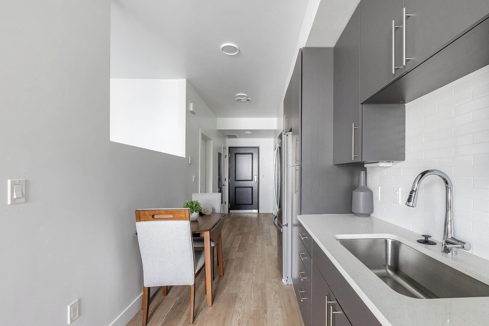 A modern kitchen with grey cabinets, a stainless steel sink, and a wooden dining table with chairs.
