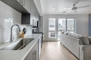 A modern kitchen with a sink, stove, and cabinets, leading to a balcony with a view of buildings. - Landing | Amazing Studio in Central City (Salt Lake City)