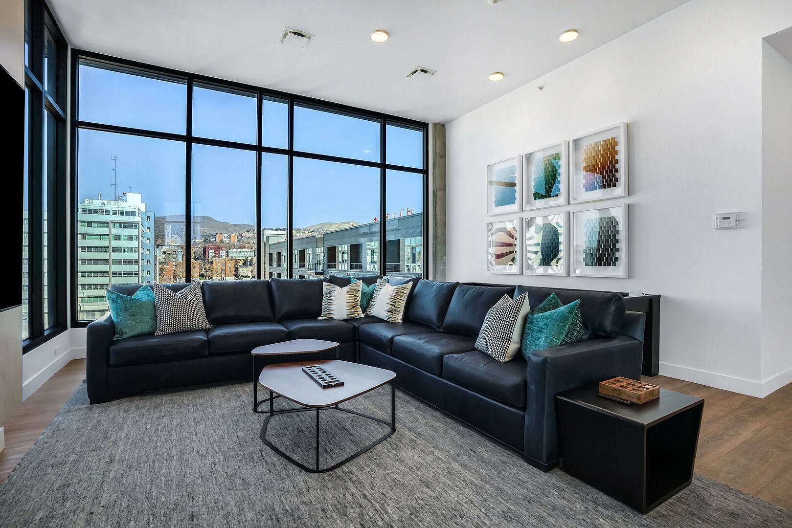 Una sala moderna con un sofá modular, una mesa de centro y vistas de la ciudad a través de amplias ventanas.