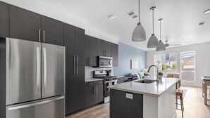 Uma cozinha moderna com armários escuros, eletrodomésticos de aço inoxidável e iluminação pendente.