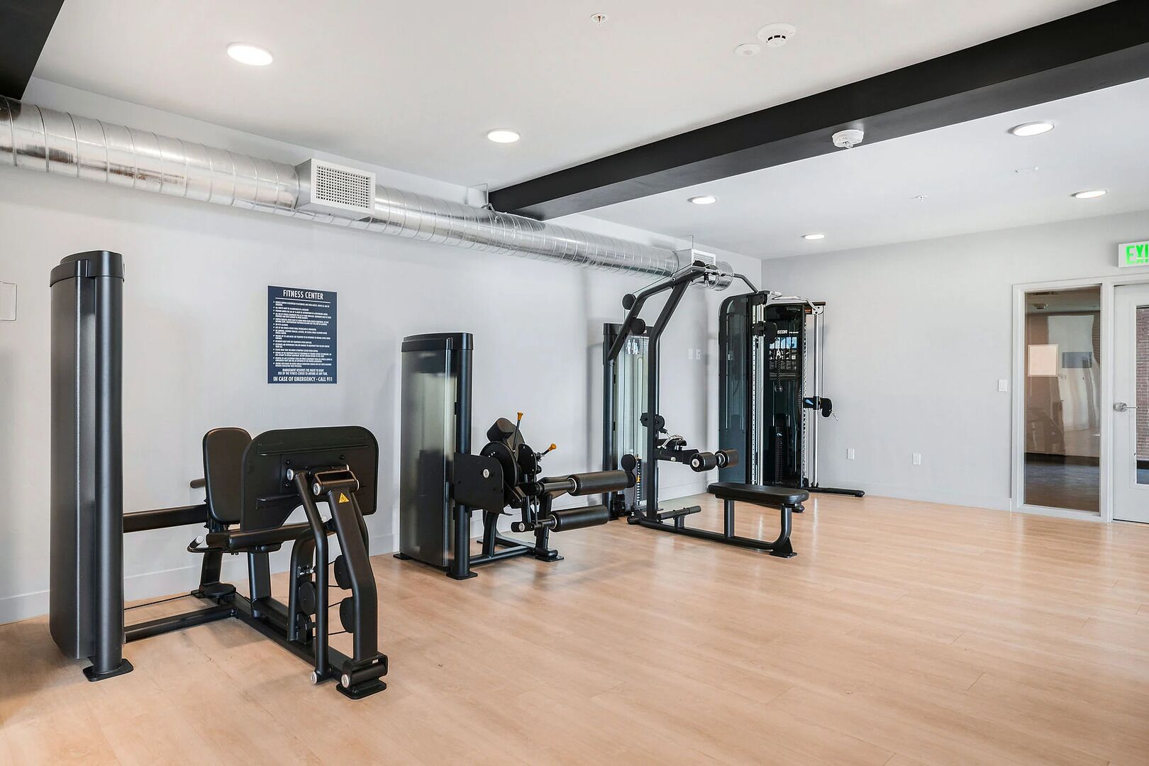 A fitness center with exercise equipment, a wall-mounted sign, and a door with an exit sign.