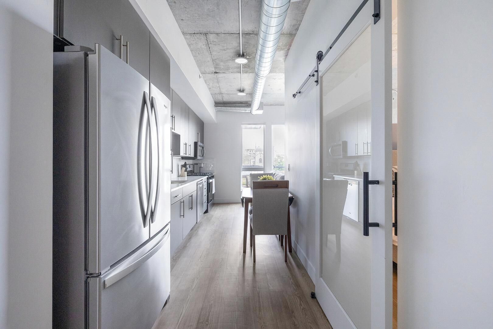 A modern kitchen with stainless steel appliances, a dining area with a table and chairs, and a view through a window.