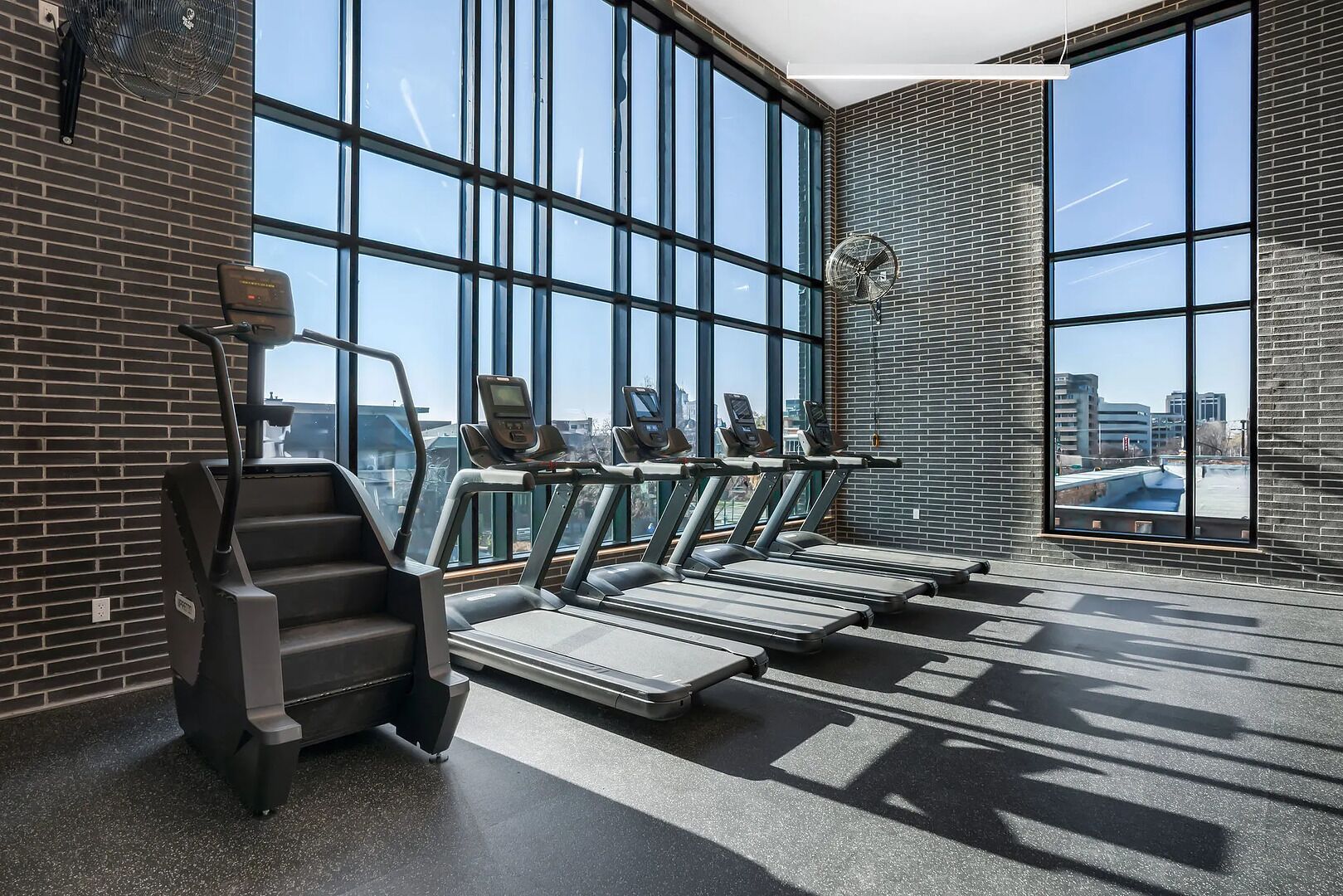 A gym with treadmills, a stair climber, and large windows offering a city view.