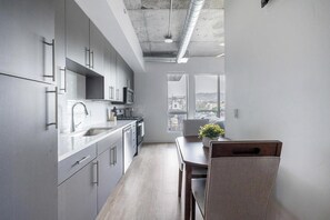 A modern kitchen with grey cabinetry, stainless steel appliances, and a view of the city through large windows. - Landing | Amazing Studio in Central City (Salt Lake City)