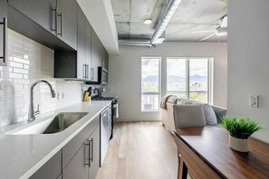 Eine moderne Küche mit großem Fenster, einem Essbereich mit Holztisch und einer Sitzecke mit Sofa.