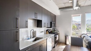 Een moderne keuken met grijze kastjes, een roestvrijstalen spoelbak en een stadszicht door grote ramen.