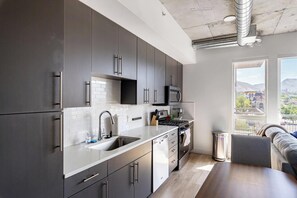A modern kitchen with grey cabinets, a stainless steel sink, and a view of the city through large windows. - Landing | Incredible Studio in Central City (Salt Lake City)