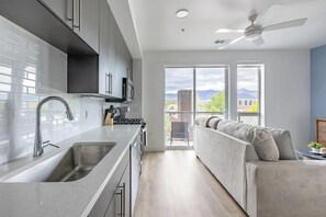 A modern kitchen with a large island, a dining area with a sofa, and a balcony with a view. - Landing | Chic Studio in Central City (Salt Lake City)