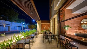 An outdoor cafe area with tables and chairs, a brick wall, and a glass window. - ROSSI TINY (Villa Mercedes)