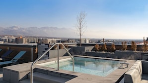 A rooftop pool with clear blue water, a metal ladder, and a view of mountains in the background. - Landing | Chic 1BD in Central City (Salt Lake City)