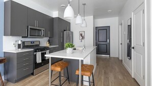 A modern kitchen with grey cabinets, a white countertop, stainless steel appliances, and a central island with stools. - Landing | Chic 1BD in Central City (Salt Lake City)
