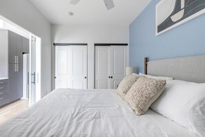 Un dormitorio con cama, cabecera, puerta y un cuadro en la pared.
