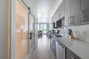 A modern kitchen with a sliding door, stainless steel appliances, and a view to a living area. - Landing | Amazing Studio in Central City (Salt Lake City)
