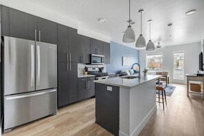A modern kitchen with dark cabinets, stainless steel appliances, and pendant lighting. - Landing | Amazing 1BD in Central City (Salt Lake City)