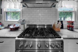 A kitchen with a stainless steel stove, white tiled backsplash, and windows with curtains. - Spacious 4-bedroom home in  Clarksville IN. accommodates 16.  gourmet kitchen.  (Clarksville)