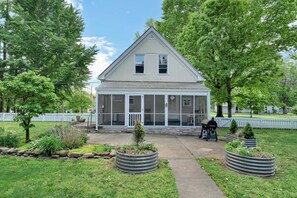 A single-story house with a covered porch, a small garden with plants in metal planters, and a clear sky. - Spacious 4-bedroom home in  Clarksville IN. accommodates 16.  gourmet kitchen.  (Clarksville)