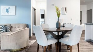 Ein modernes Wohnzimmer mit einer Couch, einem Esstisch mit Stühlen, einer Pflanze in einer Vase und einer Küche im Hintergrund.