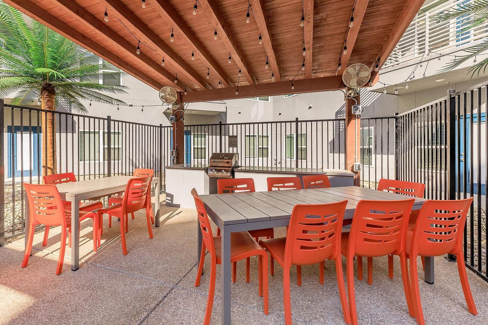 Eine Terrasse im Freien mit einer Holzpergola, einem Grill und orangefarbenen Stühlen.
