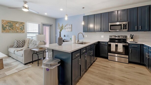 A modern kitchen with dark cabinets, stainless steel appliances, and a central island. - Landing | Amazing 1BD in Grand Prairie (Grand Prairie)