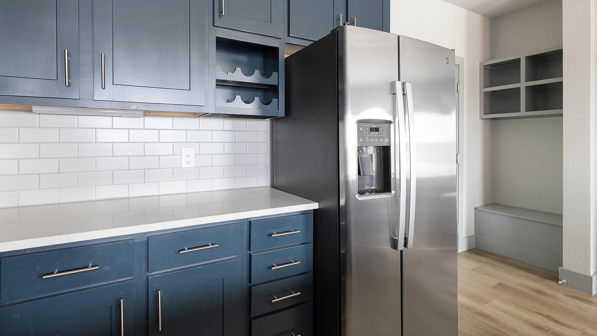 A kitchen with dark blue cabinets, a stainless steel refrigerator, and white subway tiles.