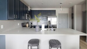 Una cocina moderna con gabinetes oscuros, una isla blanca, electrodomésticos de acero inoxidable e iluminación colgante.