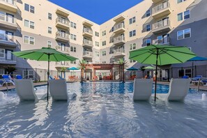 A pool area with lounge chairs and umbrellas, surrounded by a multi-story building with balconies. - Landing | Incredible 1BD in Grand Prairie (Grand Prairie)