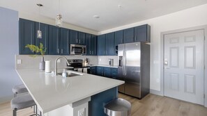A modern kitchen with dark blue cabinets, stainless steel appliances, a large island with a sink, and a white door. - Landing | Stunning 1BD in Grand Prairie (Grand Prairie)