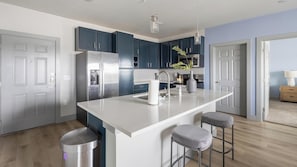 A modern kitchen with a central island, stainless steel appliances, and dark blue cabinets. - Landing | Chic 2BD in Grand Prairie (Grand Prairie)