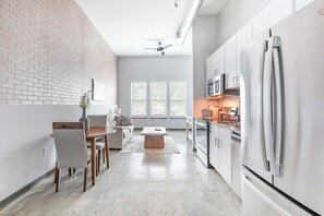 A modern kitchen with stainless steel appliances, a dining area with a table and chairs, and a living space with a sofa and a coffee table. - Landing | Stunning 1BD, Pool, Rooftop Lounge (Bellview)