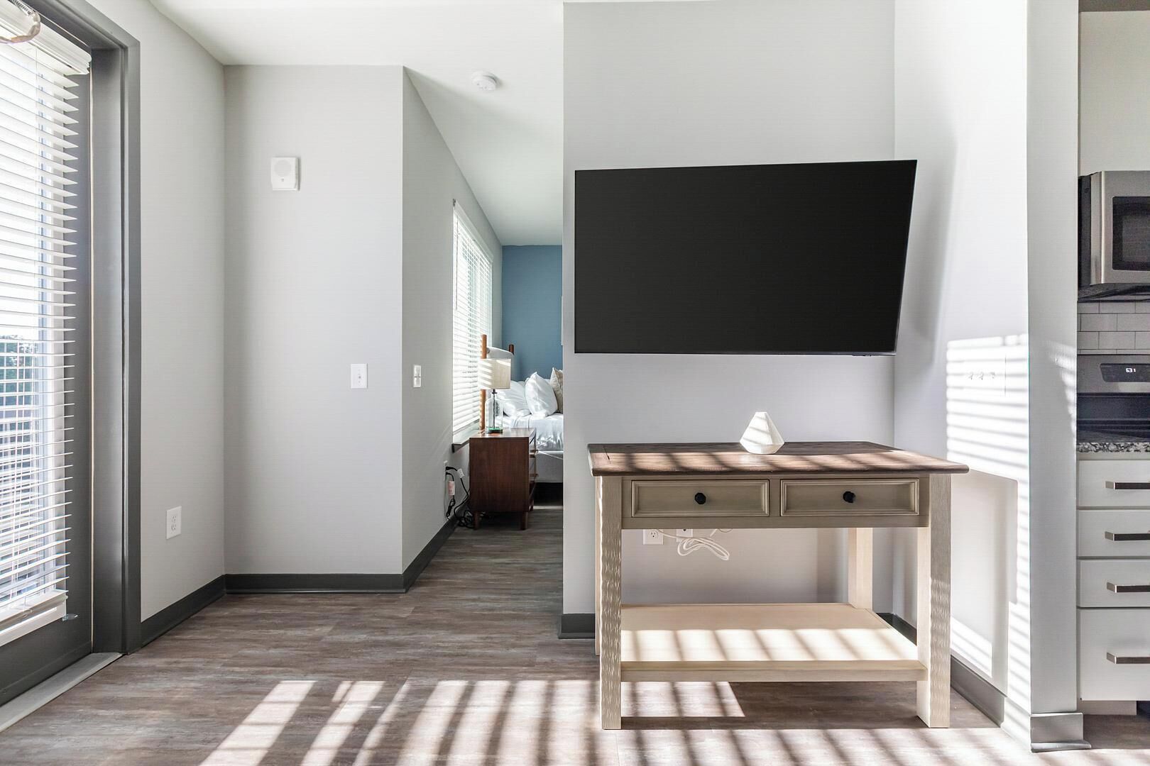 A modern hotel room with a wooden desk, a flat-screen TV, and a view of the city through the window.