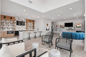 A modern kitchen with a central island, bar stools, and a seating area with patterned chairs and a blue sofa.